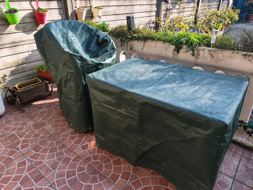 Tavolo e sedia da giardino sotto coperture verdi su misura con occhielli, in un patio piastrellato