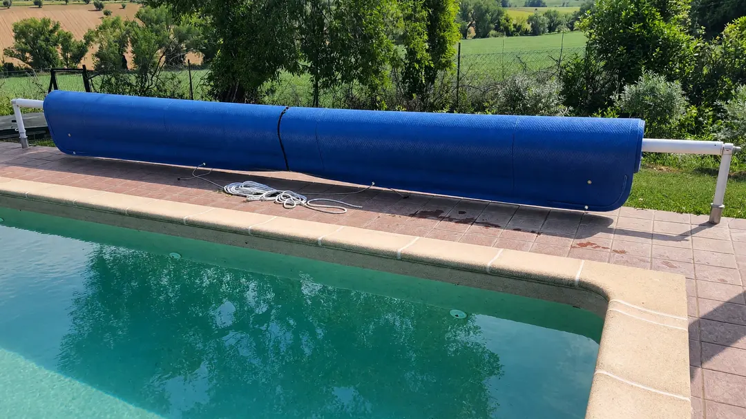 Telo a mousse blu arrotolato su un rullo con piantane, a bordo di una piscina interrata