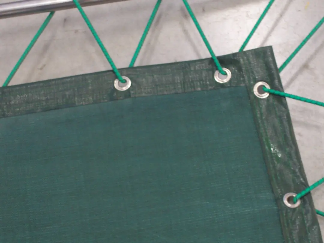 Dettaglio dell’angolo di un telo ombreggiante in rete Eltex verde, con occhielli metallici ed elastici