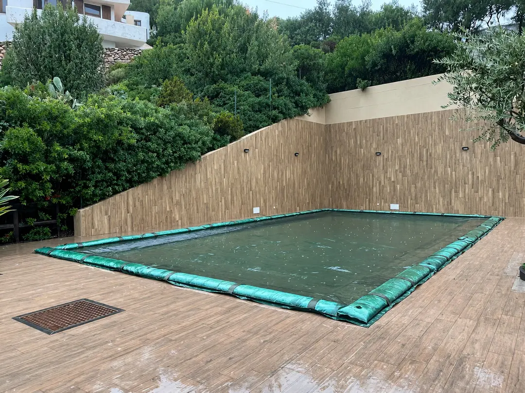 Copertura invernale verde con serbatoi su vasca rettangolare, tra un alto muro e la vegetazione